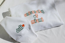 Load image into Gallery viewer, alternating thread colors of green and orange. University of Miami is embroidered with skittles font, with a second location on the cuff with the name in dark green and an orange heart next to it
